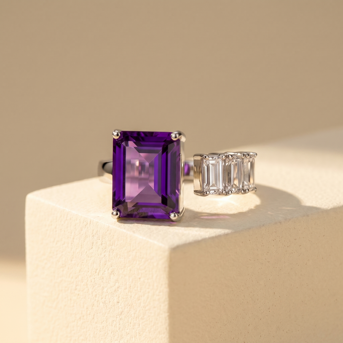 Open ring with a vibrant purple sapphire and three diamond side stones on a beige background; all gemstones are emerald cut