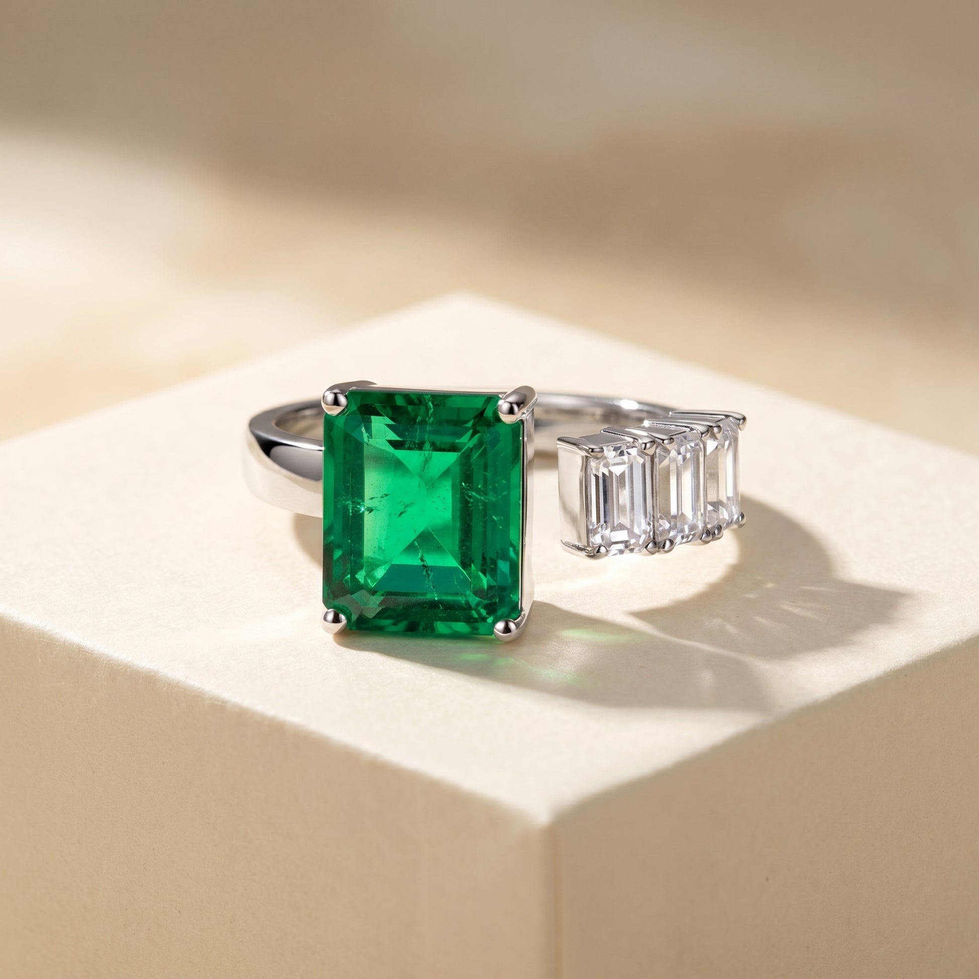 Open ring with a Colombian green emerald and three diamond side stones on a beige background; all gemstones are emerald cut