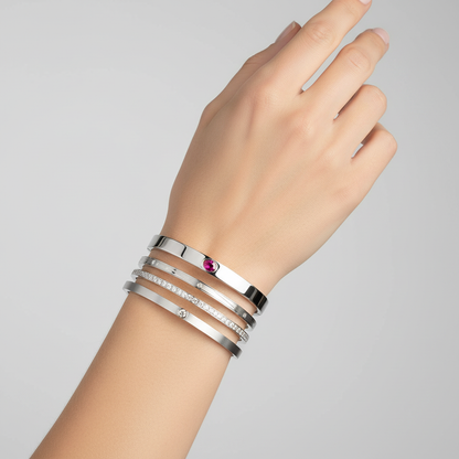 Hand wearing multiple white gold, pink sapphire and diamond bracelets on a gray background