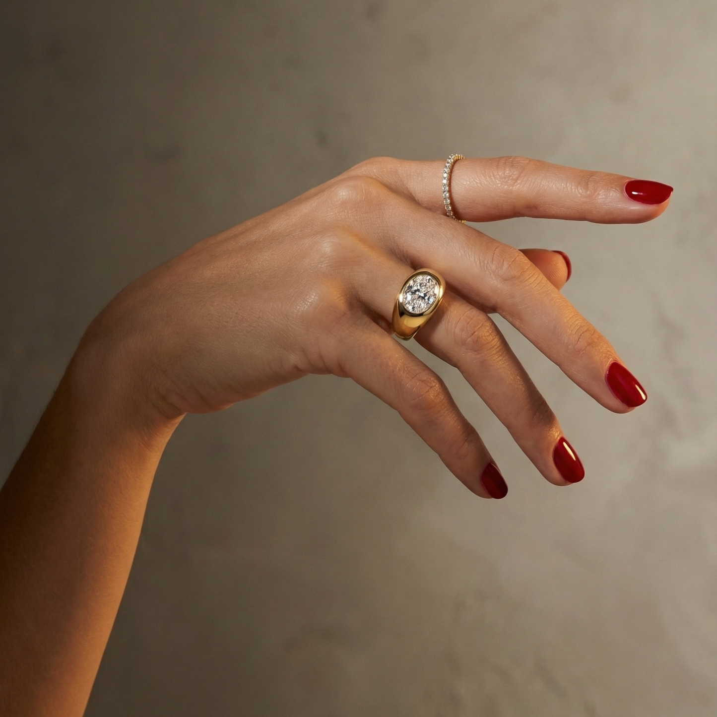 Hand wearing a statement, gold signet ring with a large oval diamond laterally set; hand shown on a plain background