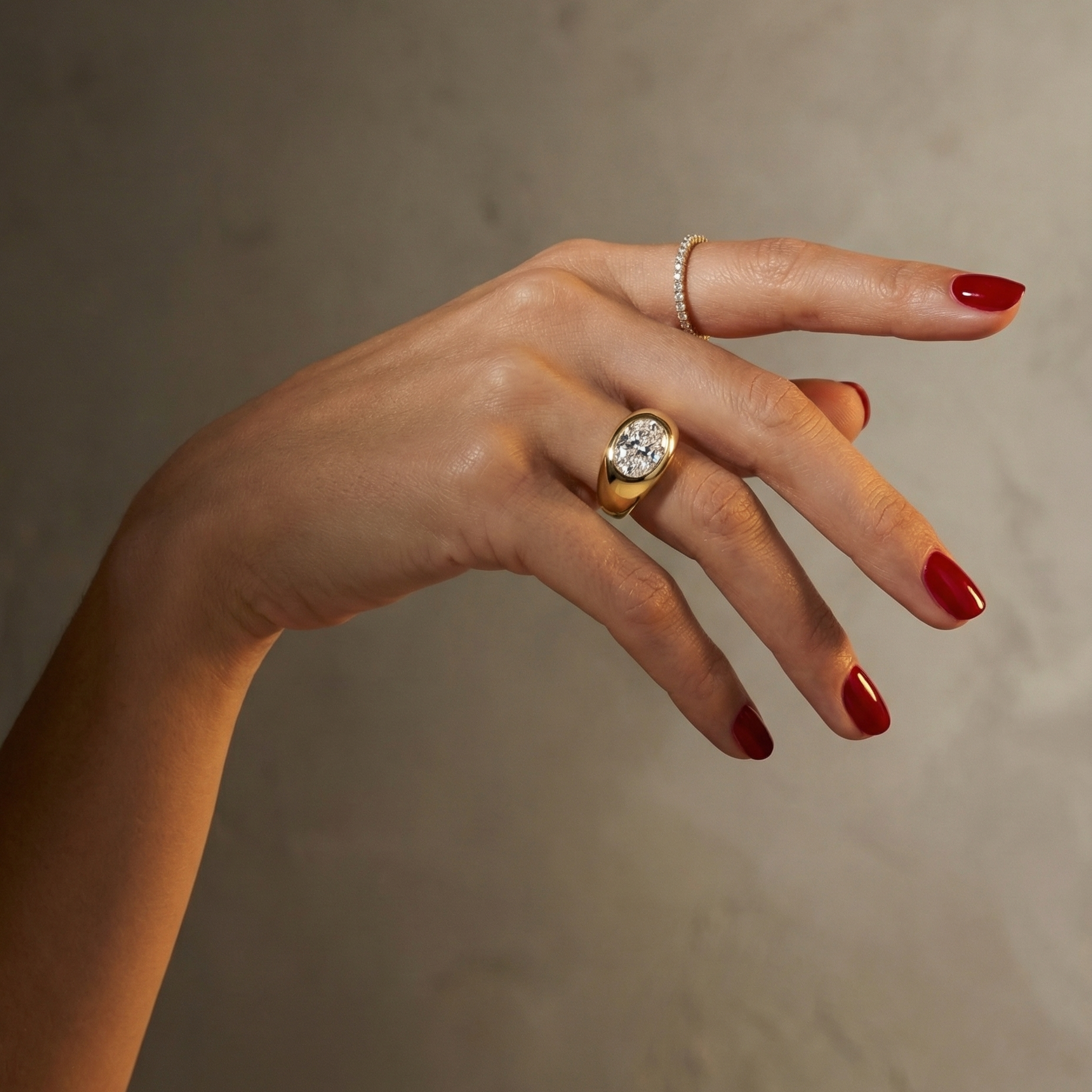 Hand wearing a statement, gold signet ring with a large oval diamond laterally set; hand shown on a plain background