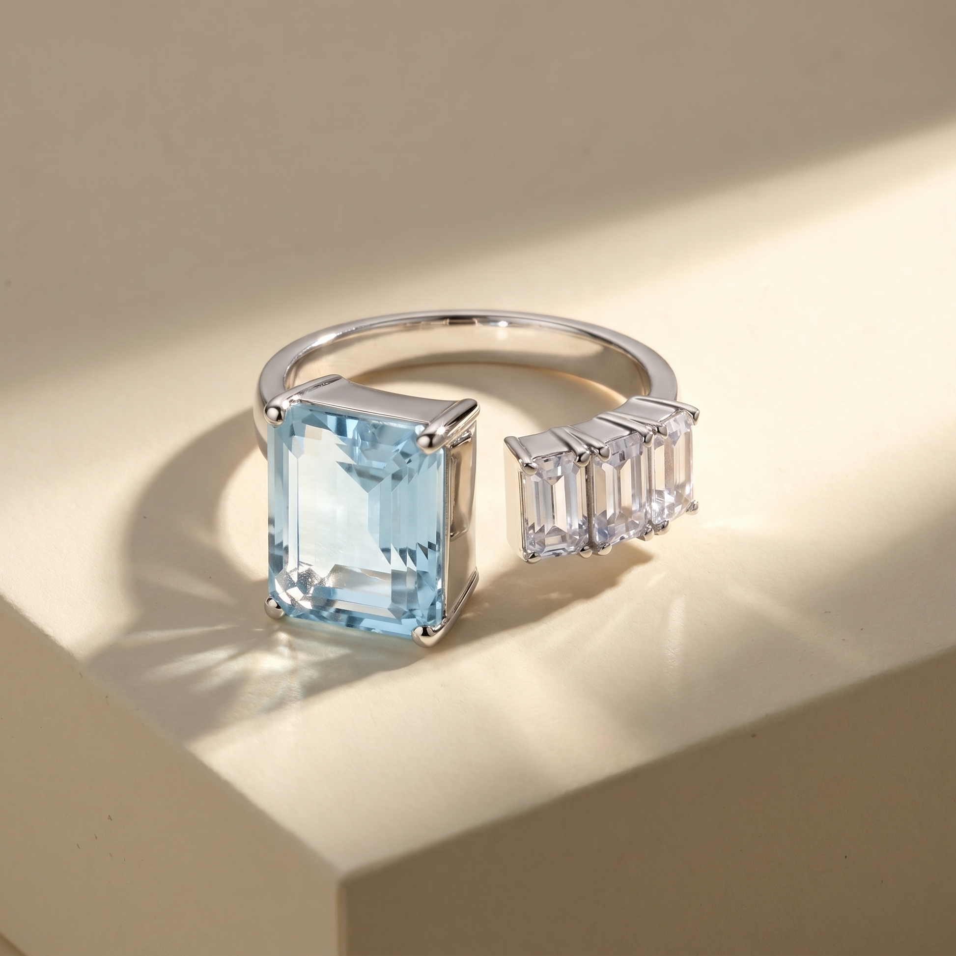 Open ring with a light aquamarine shade blue spinel and three diamond side stones on a beige background; all gemstones are emerald cut