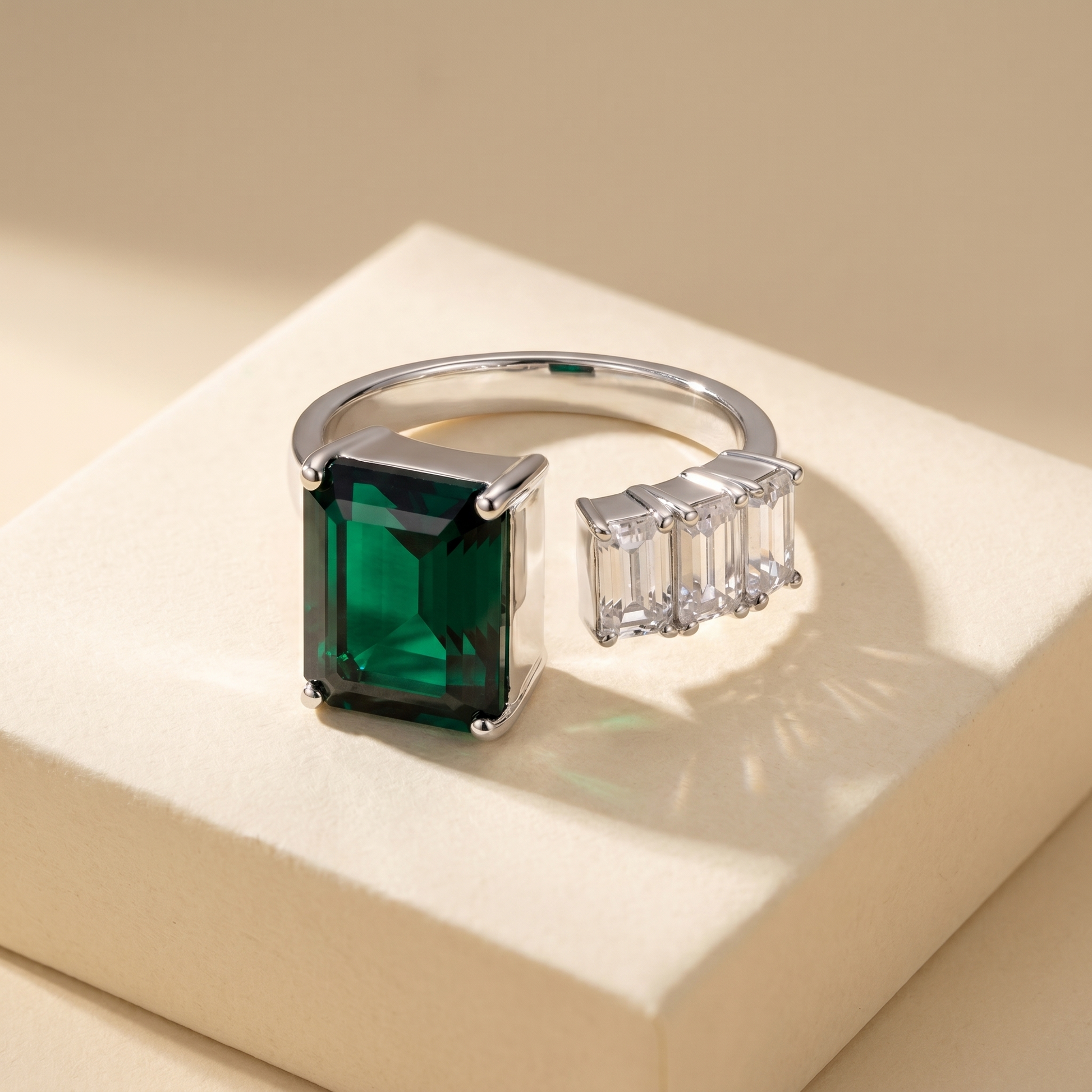 Open ring with a Zambian green emerald and three diamond side stones on a beige background; all gemstones are emerald cut