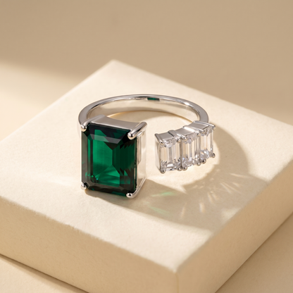 Open ring with a Zambian green emerald and three diamond side stones on a beige background; all gemstones are emerald cut