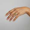 Hand wearing a gold signet style ring with a green Colombian Emerald round gemstone on a neutral background