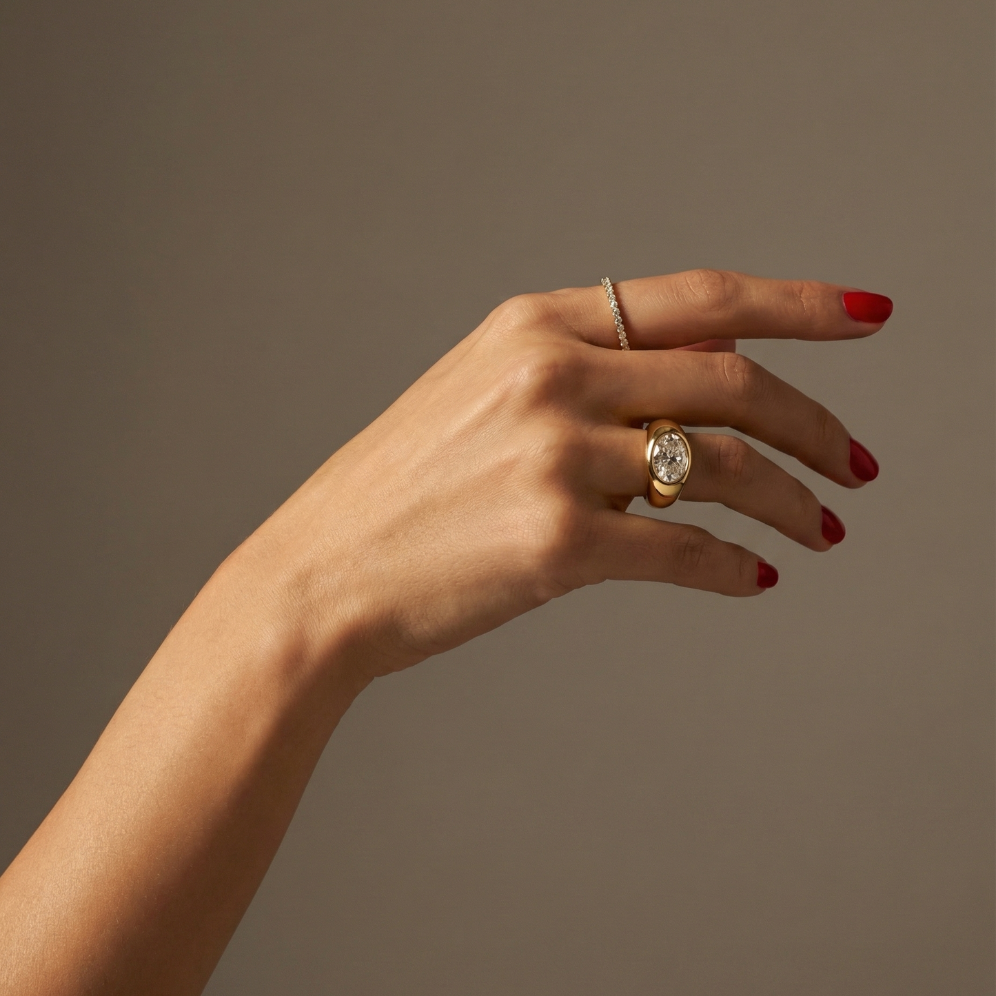 Hand wearing a statement, gold signet ring with a large oval diamond laterally set; hand shown on a plain background