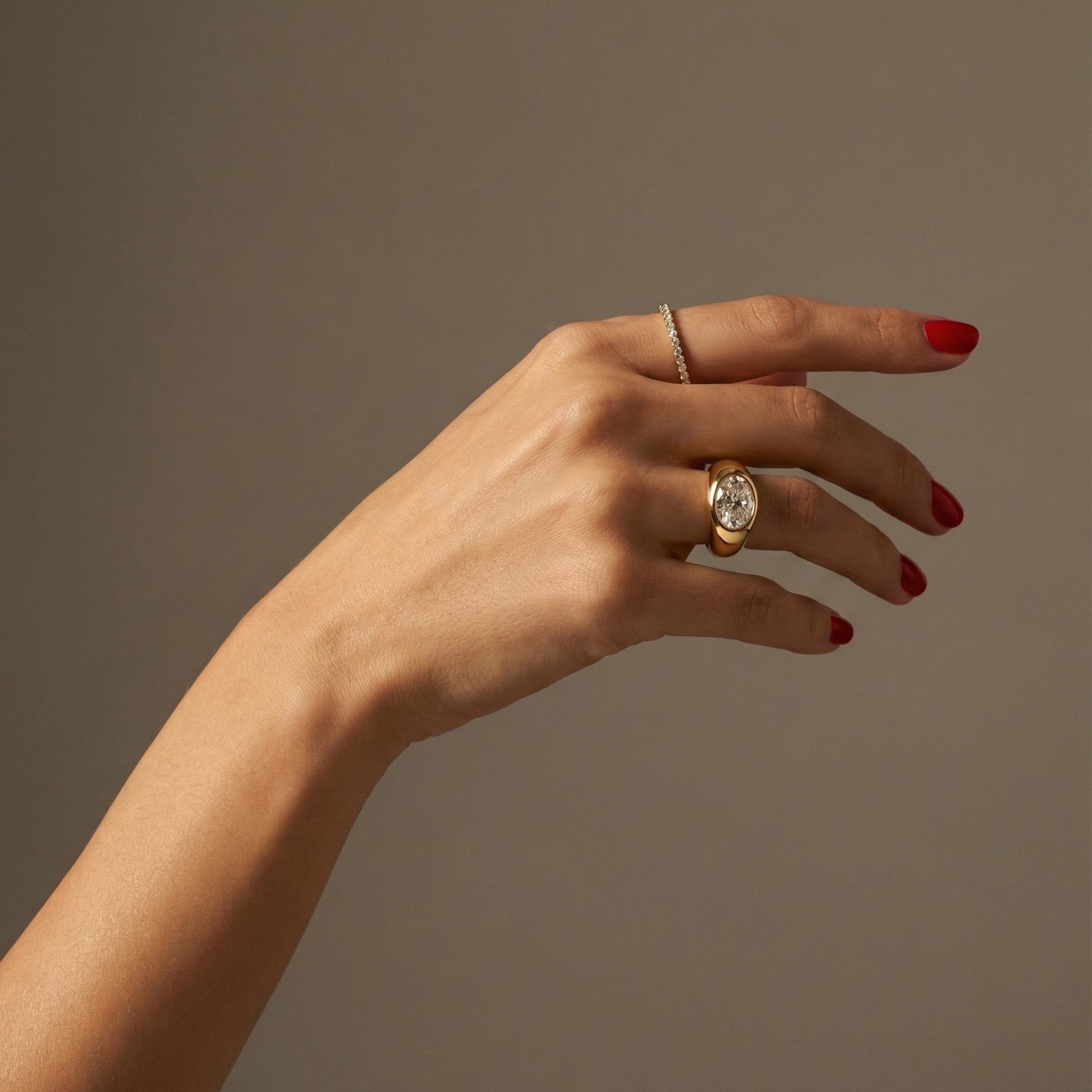 Hand wearing a statement, gold signet ring with a large oval diamond laterally set; hand shown on a plain background