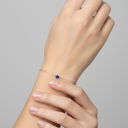 Chain solitaire bracelet with a pear cut blue sapphire on a hand against a gray background