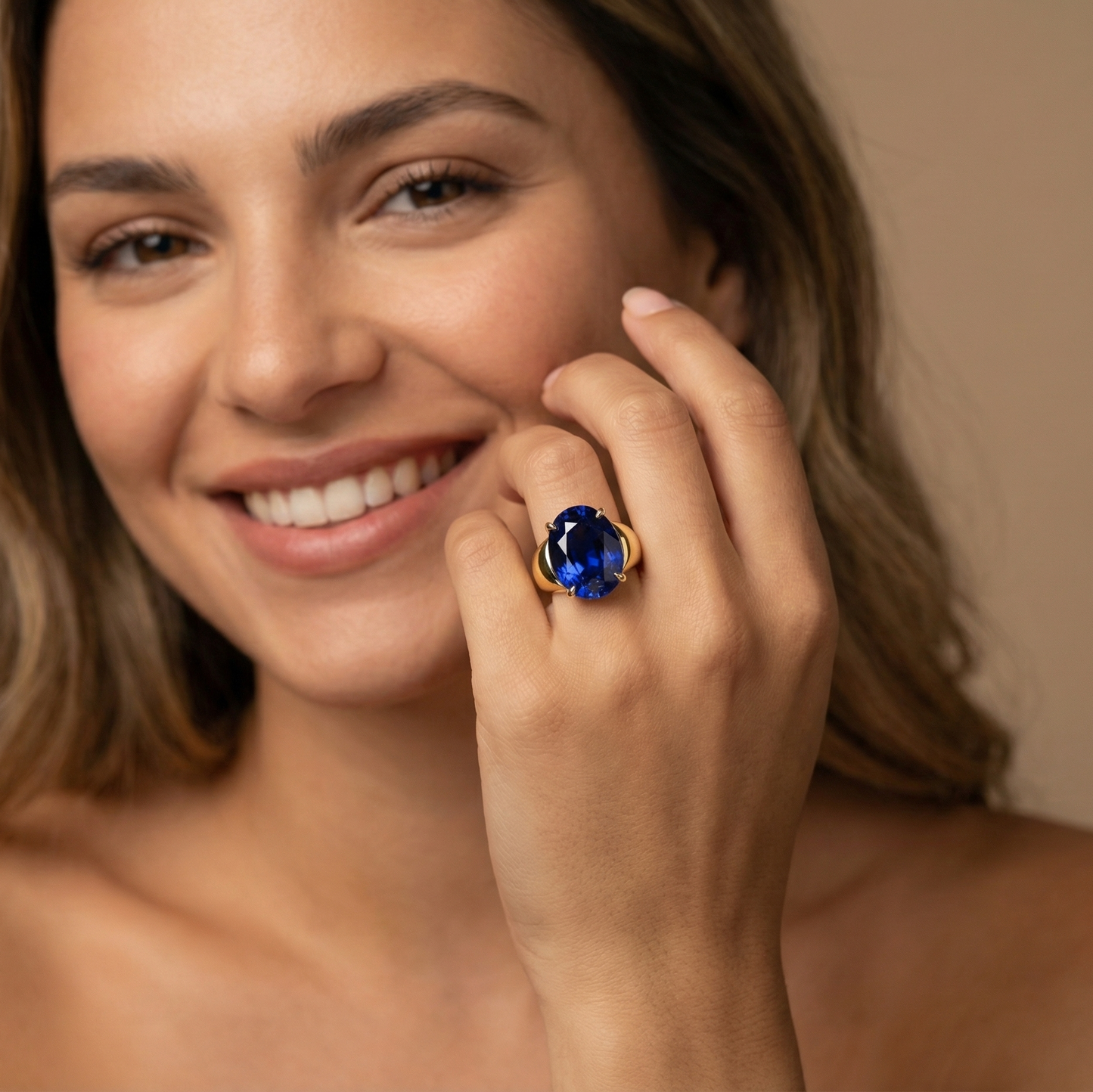 Woman wearing a gold large signet ring with an oval blue sapphire on a neutral background